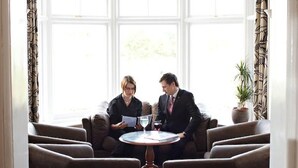 A room with a curved window, two armchairs, a small round table, and a potted plant. - The Links Country Park Hotel (Cromer)