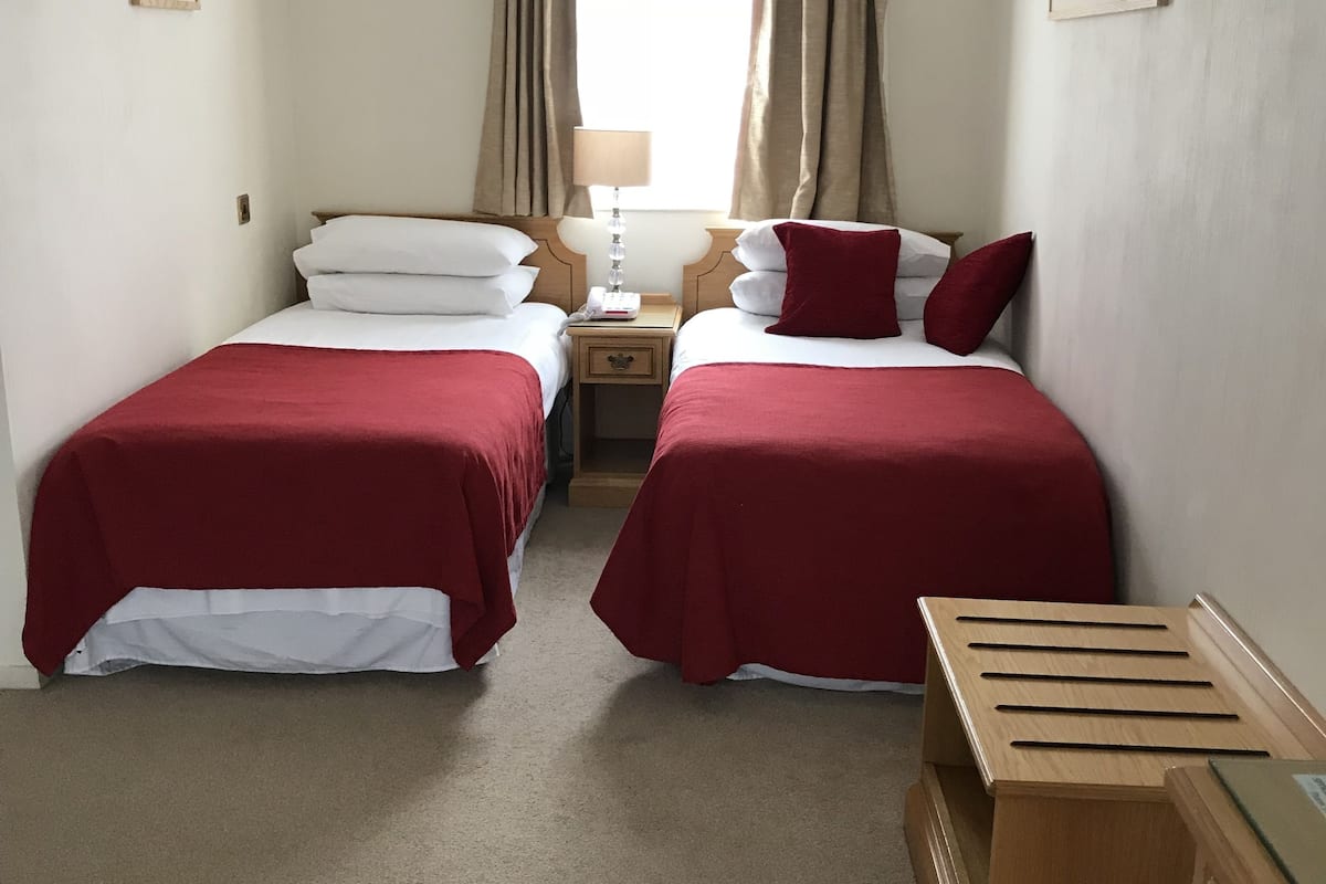 A hotel room with two beds, each with red bedding, a wooden nightstand with a lamp, and a small wooden dresser.
