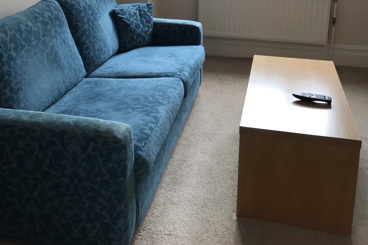 A living room with a blue sofa, a wooden coffee table, and a window with curtains.