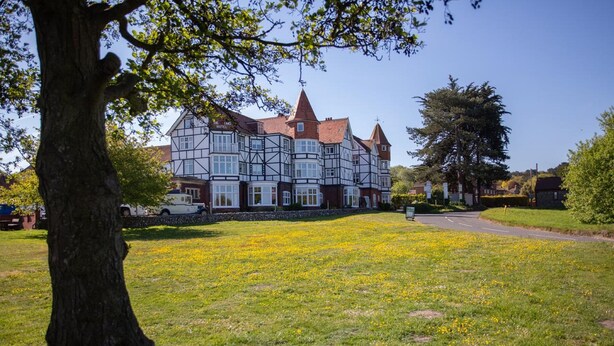 A large, traditional building with multiple windows and a prominent tower, surrounded by a grassy area with yellow flowers.