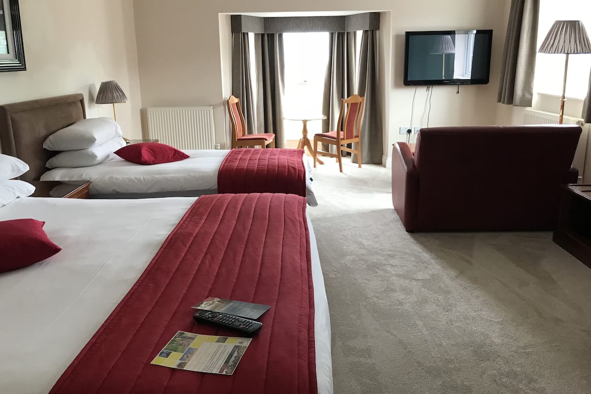 A hotel room with two beds, a sofa, a TV, and a dining area with chairs and a table.