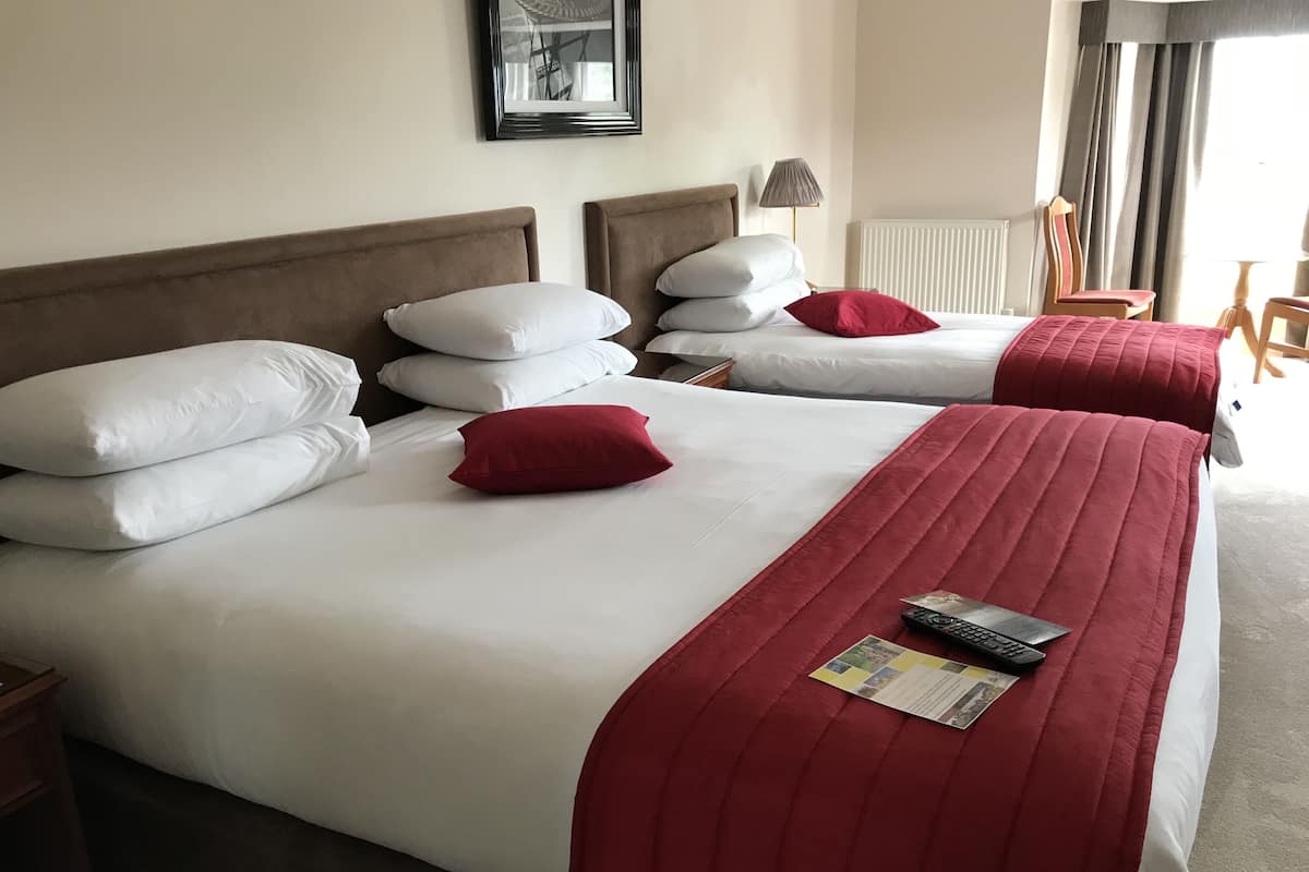 A hotel room with two beds, each with white bedding and red pillows. There is a framed picture on the wall, a lamp, and a chair.