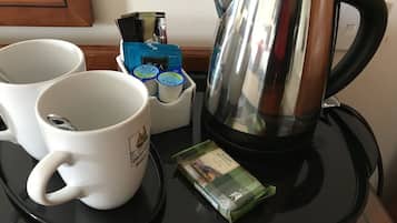 Una encimera de cocina con una cafetera, dos tazas blancas, un hervidor y bolsitas de té.