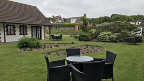 A patio area with a round table and four chairs, surrounded by a well-maintained lawn and garden beds.