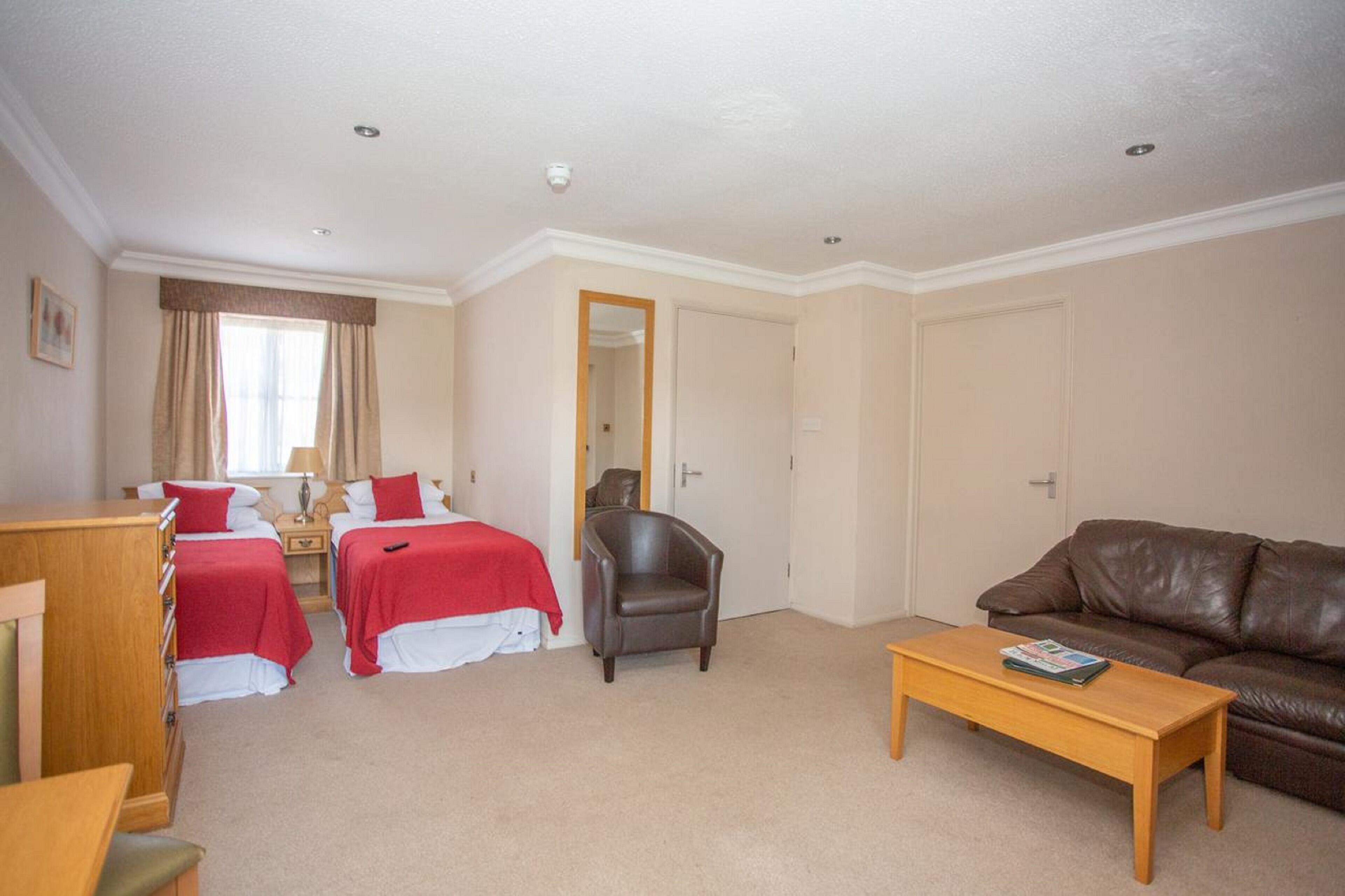 A hotel room with two beds, a leather armchair, a brown leather sofa, and a wooden coffee table.