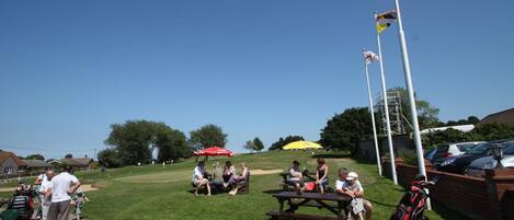 A grassy outdoor area with picnic tables, a golf cart, and flags.