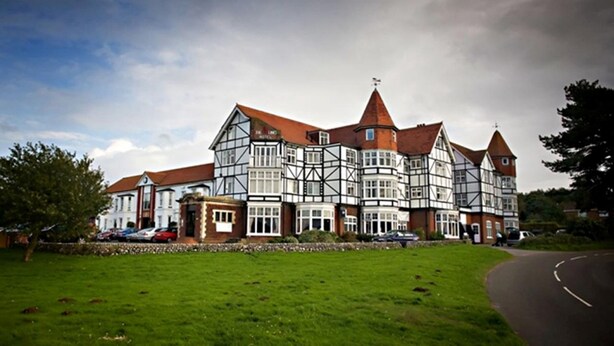 A large, historic building with multiple wings and a prominent tower, surrounded by a well-maintained lawn and a curved road. - The Links Country Park Hotel (Cromer)