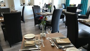A dining area with a table set for two, featuring a vase with a single red rose, salt and pepper shakers, and a wine glass. - The Links Country Park Hotel (Cromer)