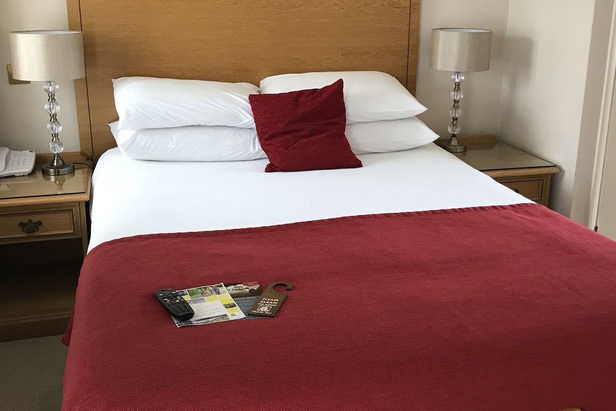 A neatly made bed with white and red bedding, a wooden headboard, and a small wooden table beside it.