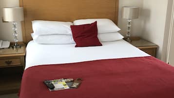 Una cama bien hecha con ropa de cama blanca y roja, un cabecero de madera y una pequeña mesita de noche a su lado.
