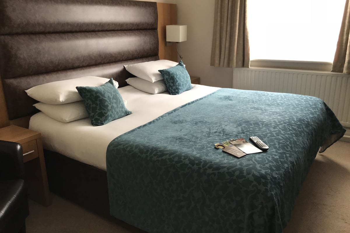 A neatly made bed with a dark headboard, white linens, and teal patterned pillows.