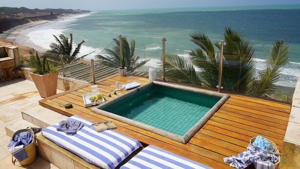 A wooden deck with a pool, lounge chairs, and a view of the ocean. - Kilombo Villas & Spa (Tibau do Sul)