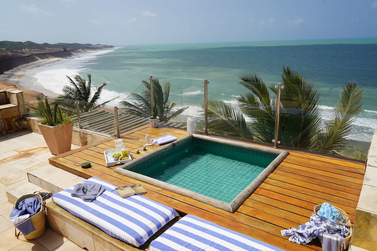 Terraza de madera con piscina, sillas de descanso y vista al océano.