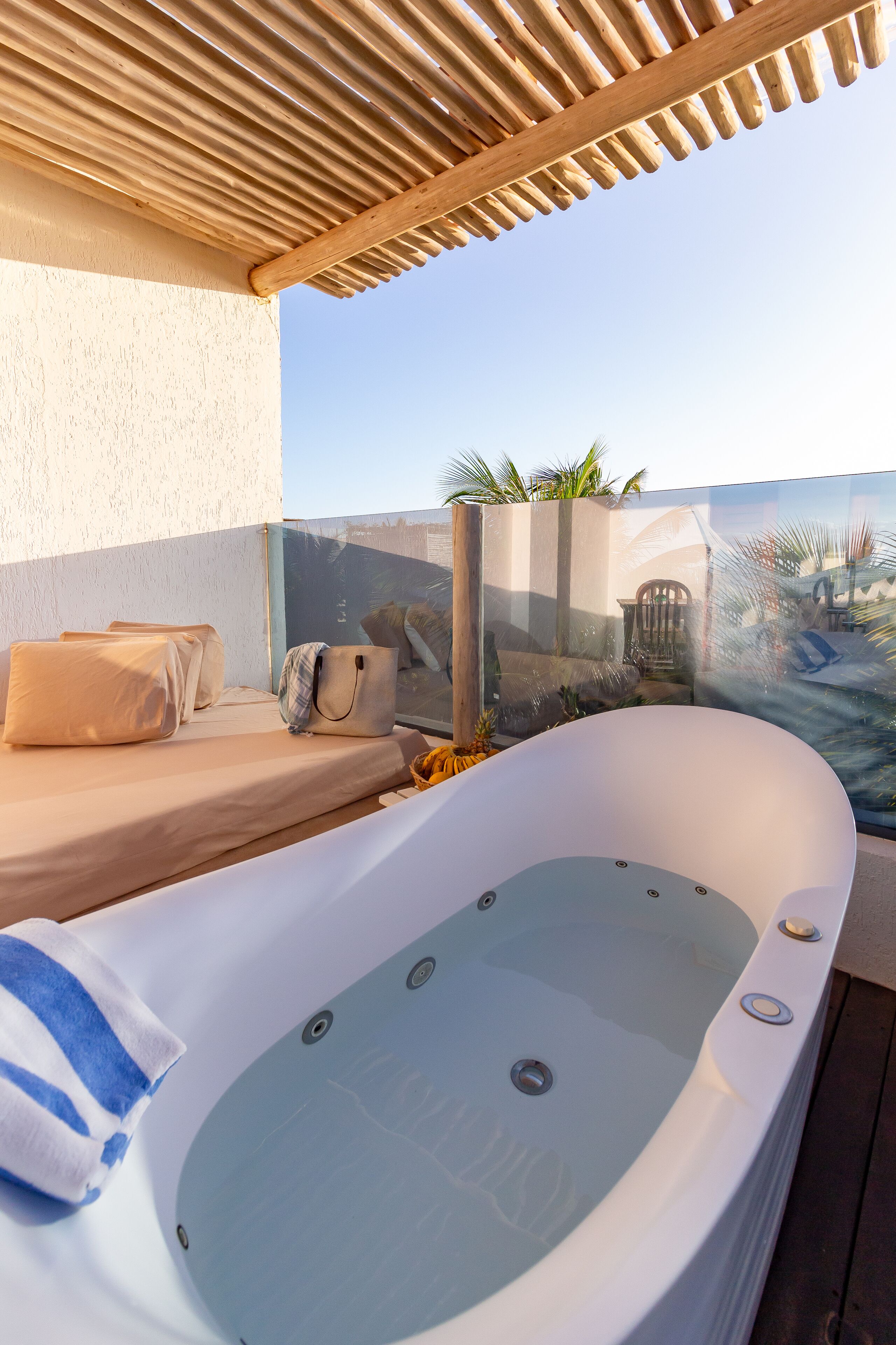 Un jacuzzi con barandilla de vidrio, una pérgola de madera y vista al mar.