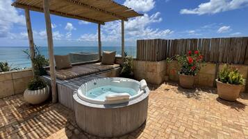 A wooden deck with a hot tub, seating area, and potted plants.