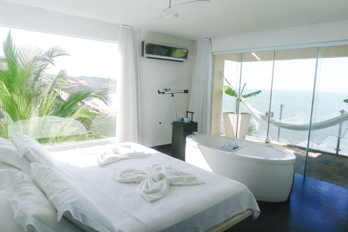 Habitación de hotel con cama, bañera y vista al océano.