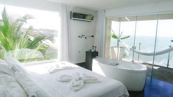 Habitación de hotel con cama, bañera y vista al océano.
