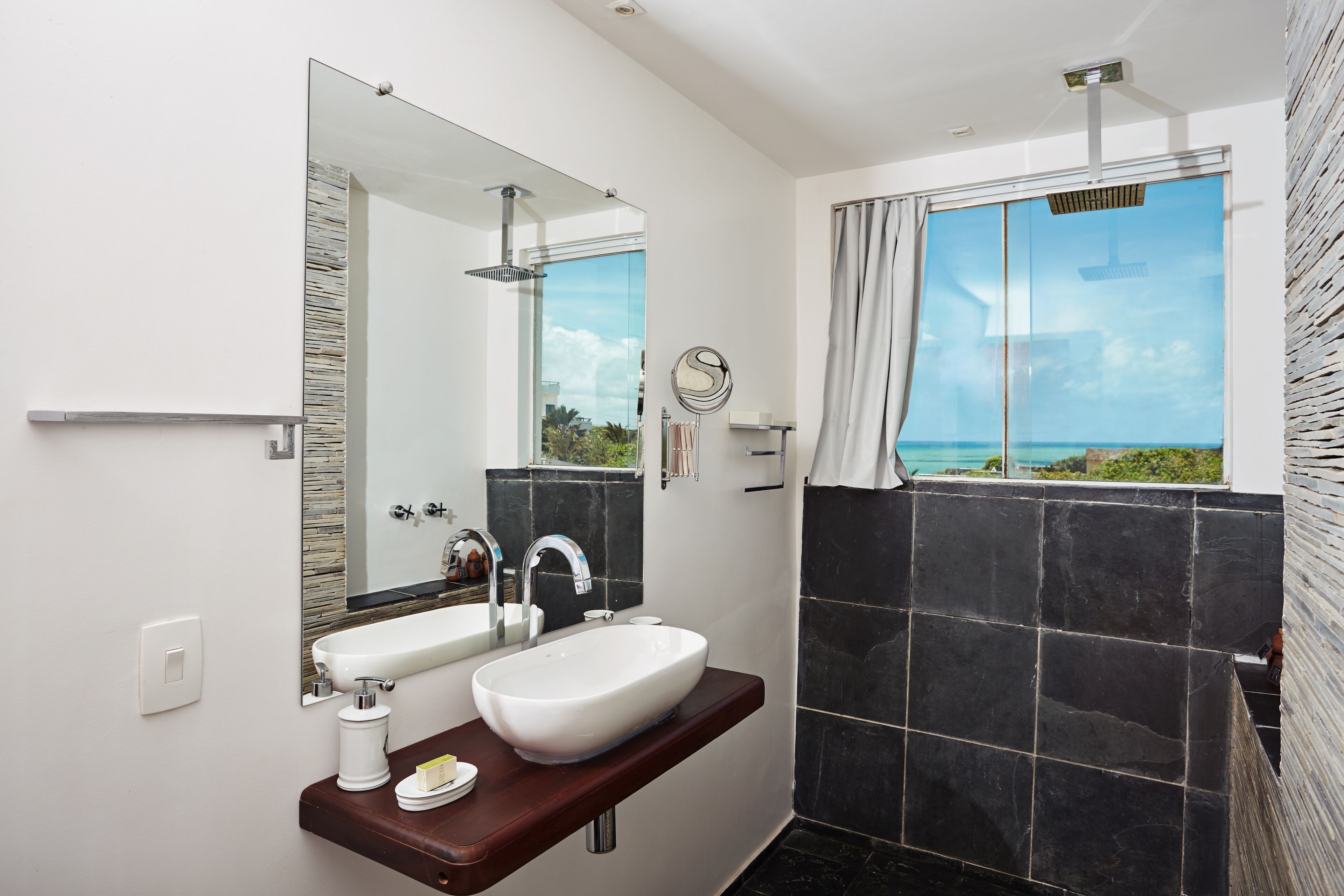 Une salle de bain moderne avec un grand miroir, deux lavabos, une douche et une vue sur l’océan.