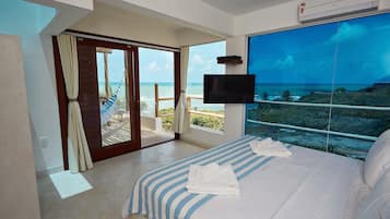 Una habitación de hotel con una cama grande, televisión y balcón con vistas al océano.