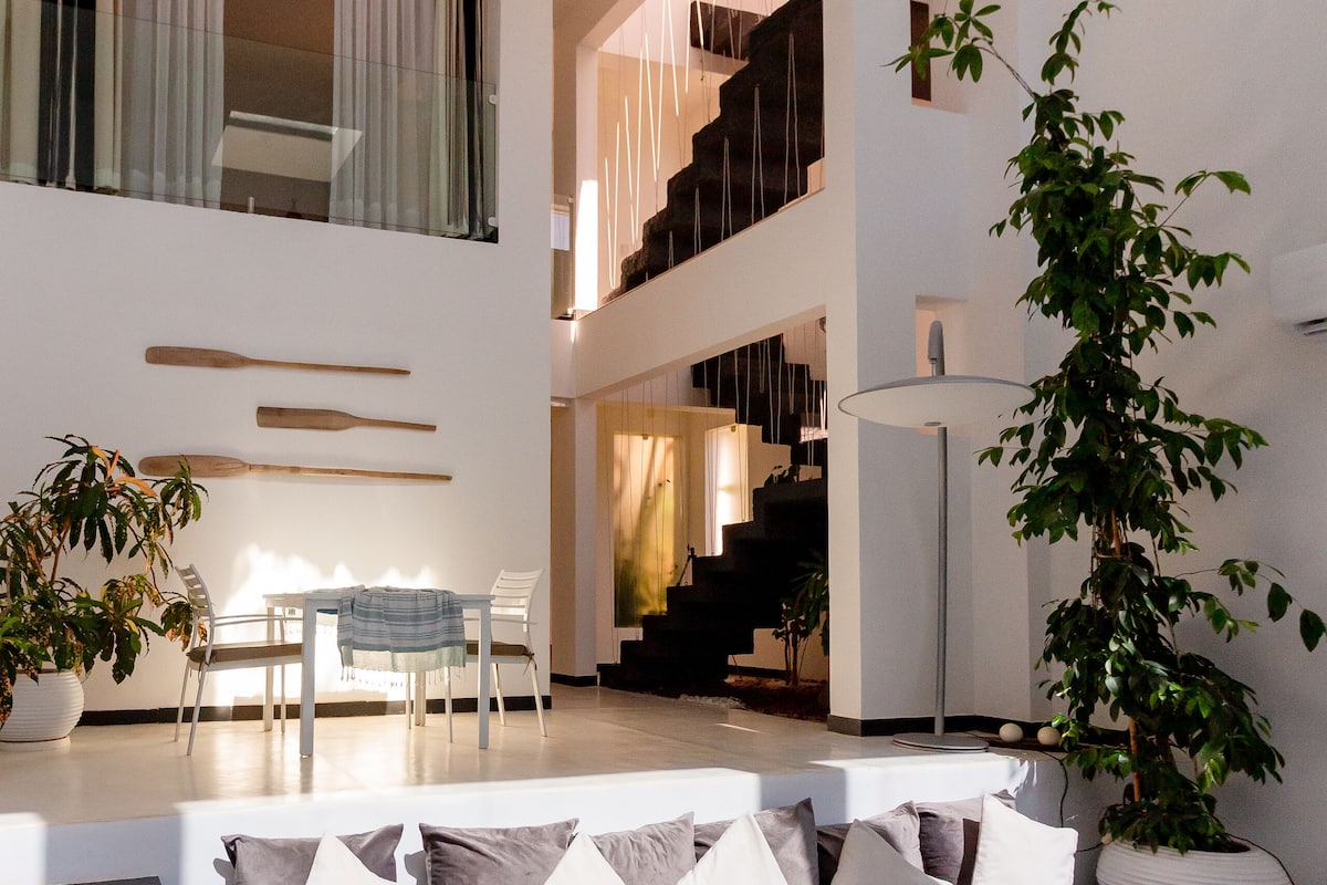 Una sala de estar moderna con un sofá modular, un comedor y una escalera que sube a un nivel superior.