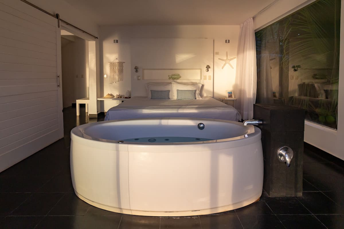Un dormitorio moderno con una bañera de hidromasaje circular grande, una cama con cabecero y una decoración de estrella de mar en la pared.