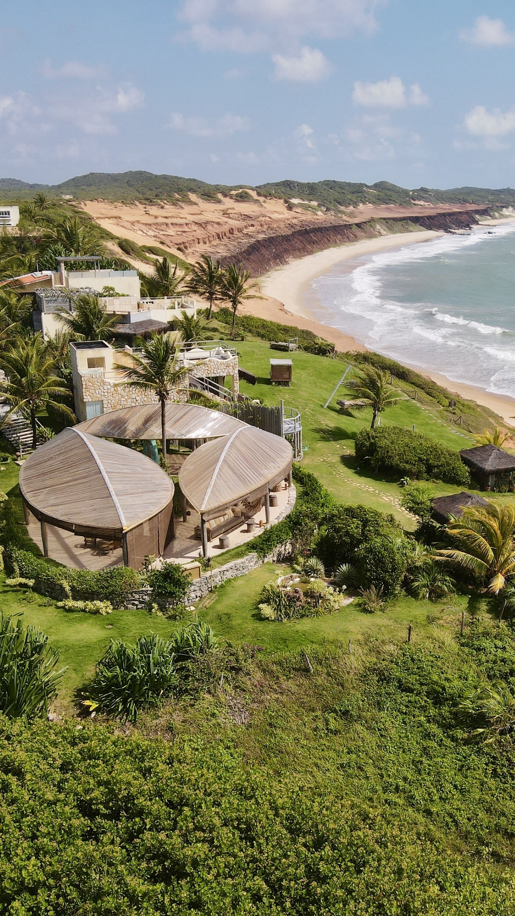 Ein Küstenresort mit mehreren bungalowsartigen Gebäuden, einem Strand und üppiger Vegetation.