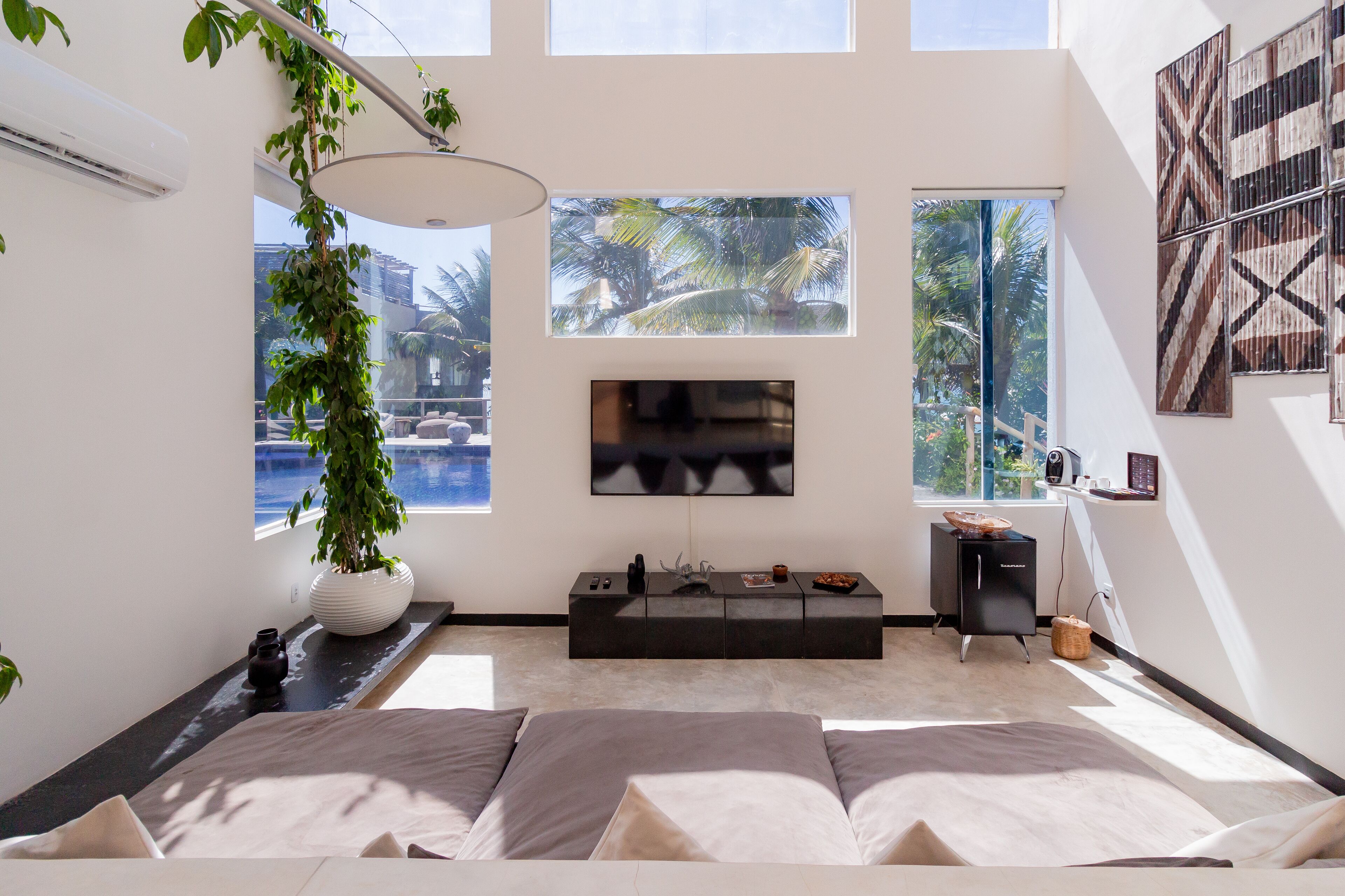 A modern living room with a large flat-screen TV, a black entertainment unit, and a large window with a view of palm trees.