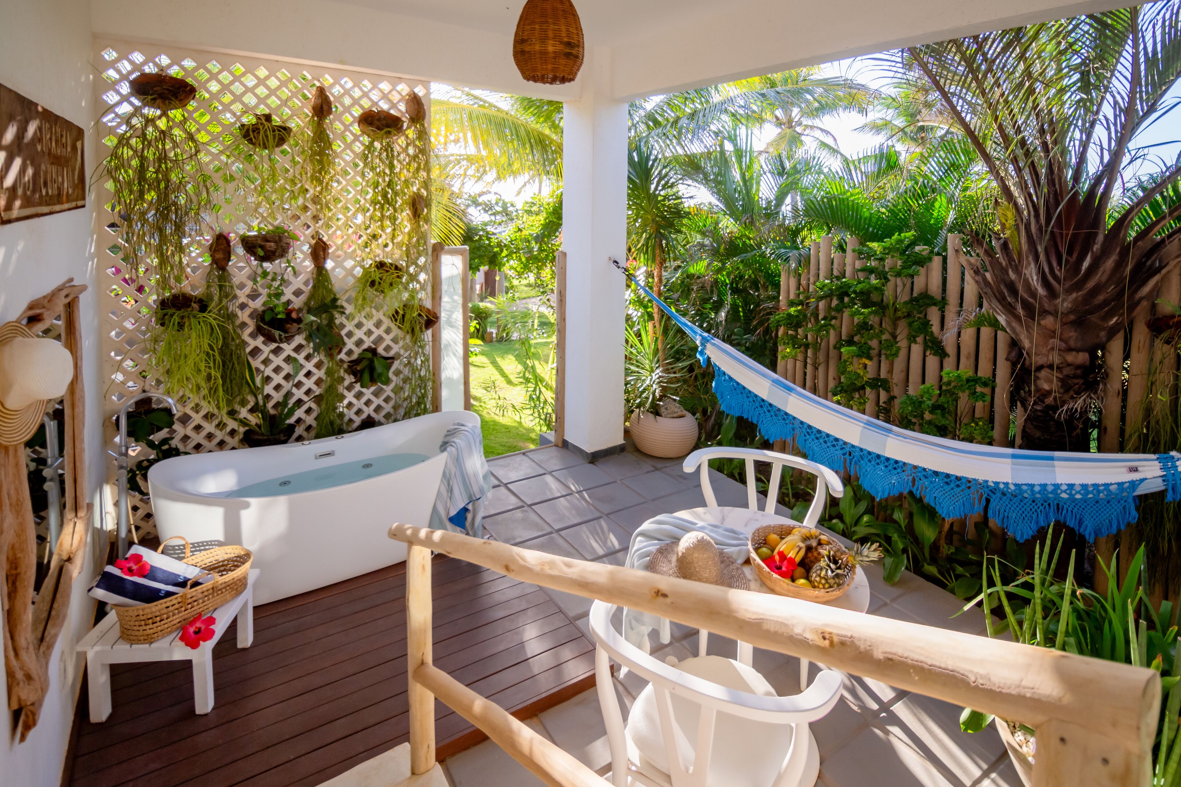 A spa area with a bathtub, a wooden deck, a hammock, and a view of lush greenery.