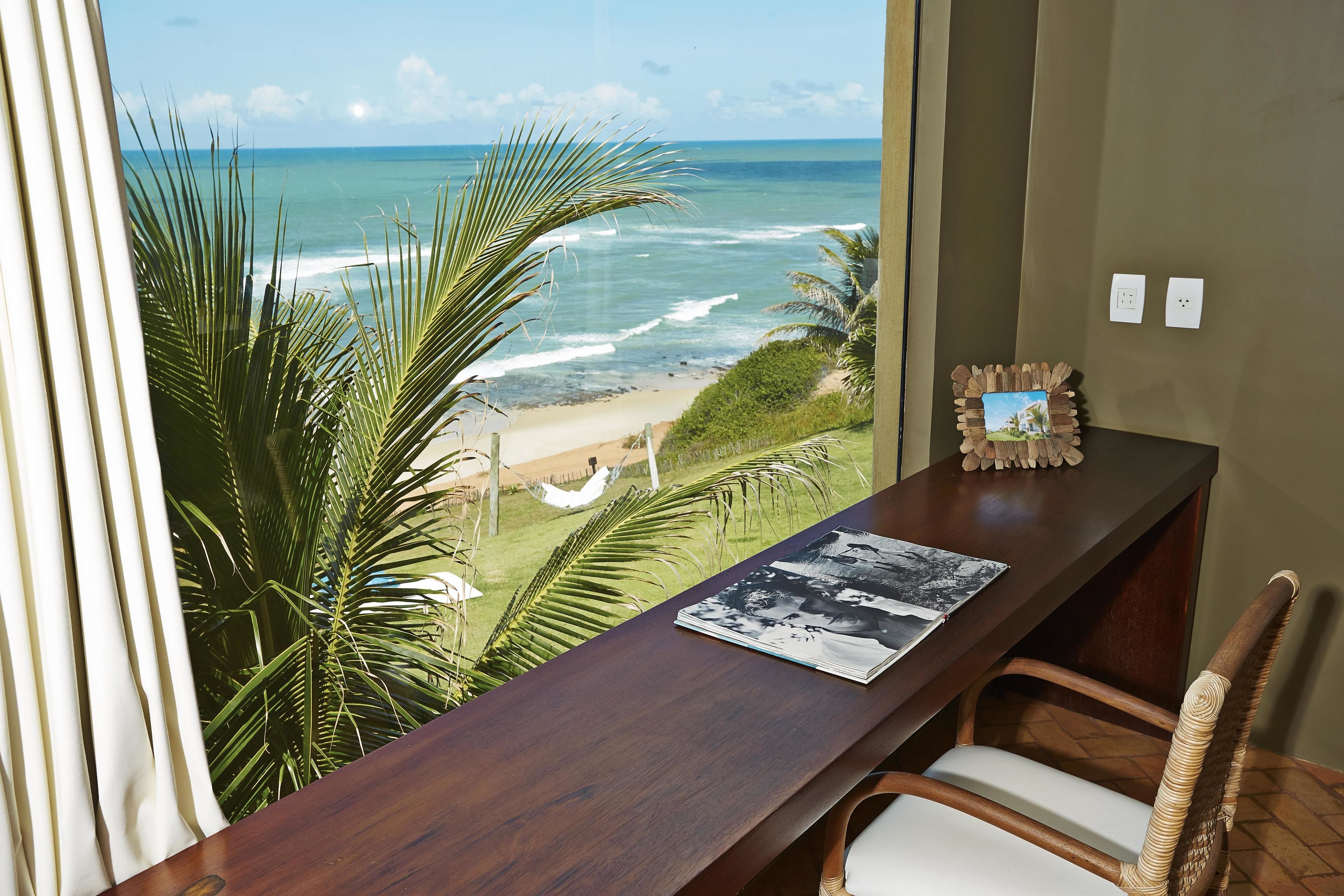 Ein Zimmer mit einem Holztisch, einem Stuhl und Blick auf das Meer.