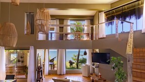 A spacious, multi-level living area with large windows, a wooden staircase, and a view of the outdoors. - Kilombo Villas & Spa (Tibau do Sul)