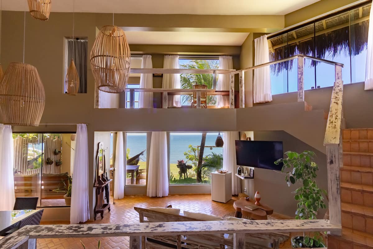 Un espacio habitable amplio, distribuido en varios niveles, con ventanas grandes, una escalera de madera y vistas al exterior.