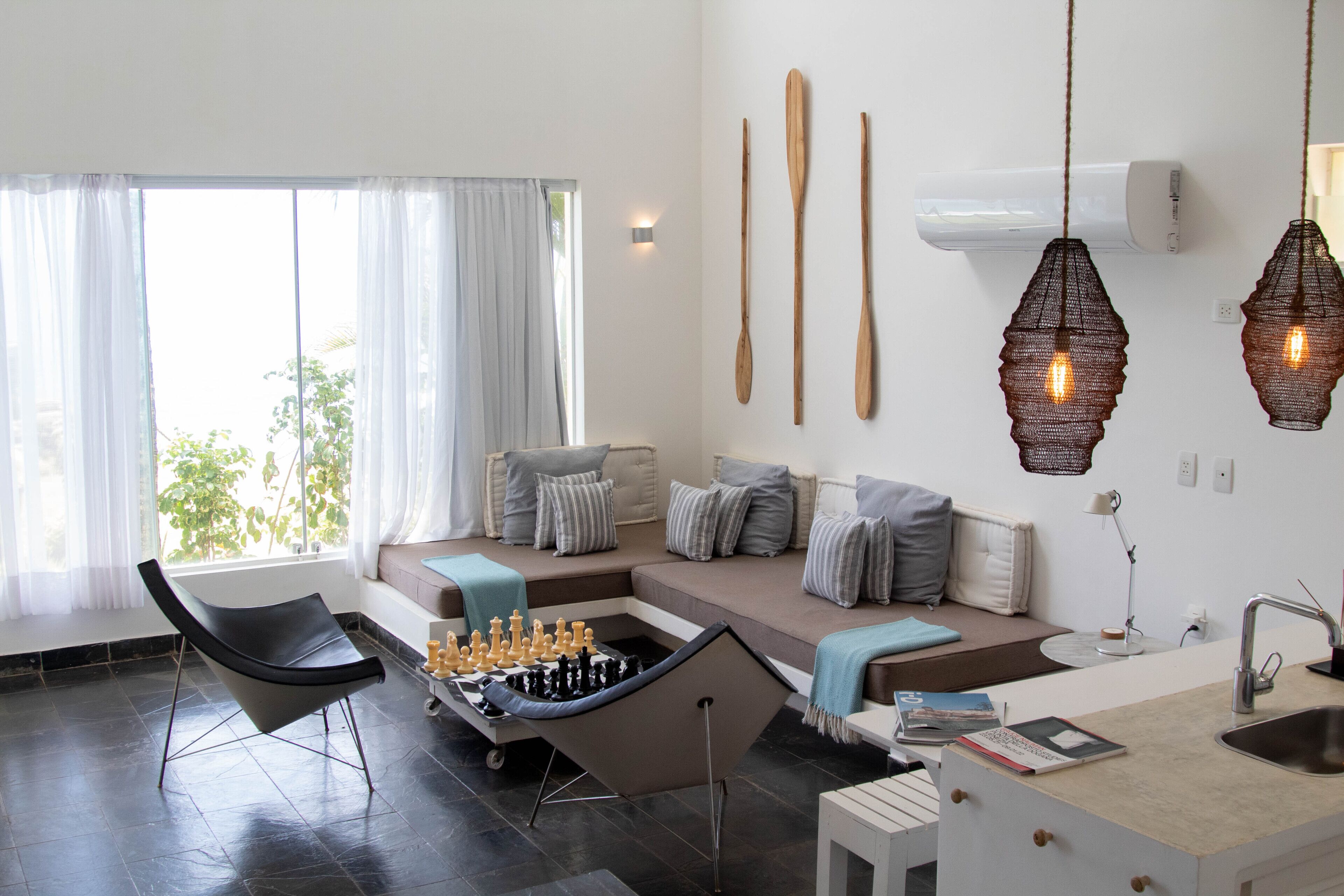 A modern living room with a sofa, a chess table, and a kitchen area with a sink and countertop.