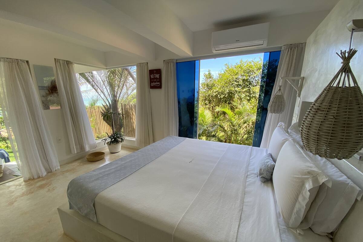 Un dormitorio con una cama grande, vistas a la vegetación exterior y un ventilador de techo.