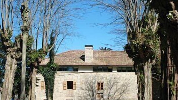 A stone building with a tiled roof, surrounded by trees and a stone pathway. - Casa Grande da Capellanía (Padron)