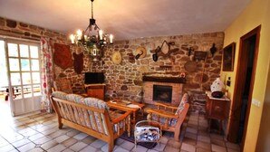 A cozy living room with a stone wall, a fireplace, and a chandelier. - Casa Grande da Capellanía (Padron)
