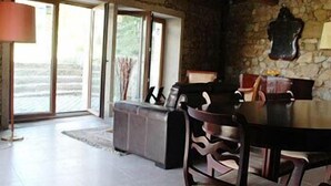 A rustic dining area with a stone wall, wooden ceiling beams, and a large table with chairs. - Casa Grande da Capellanía (Padron)