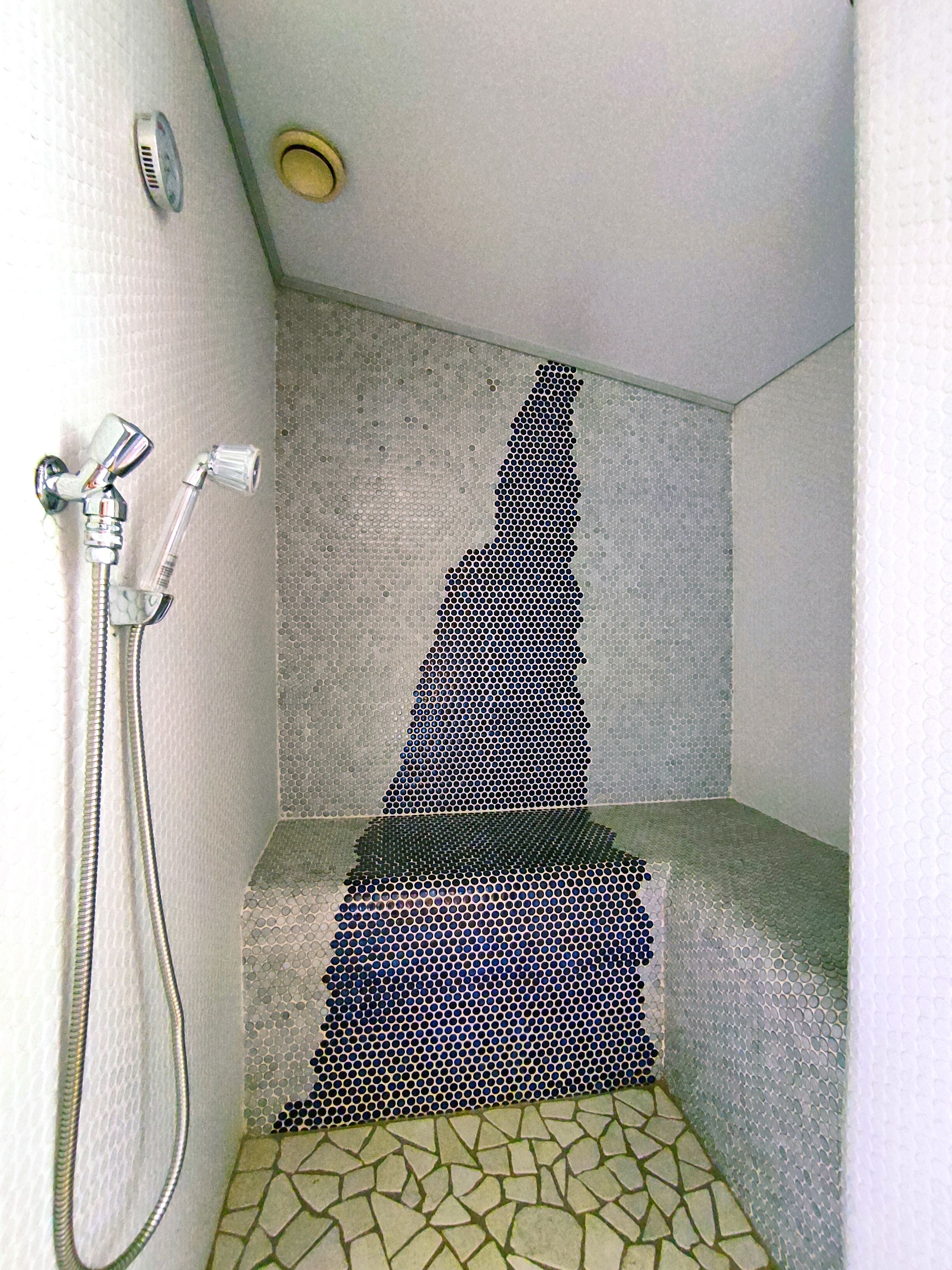 Une douche avec un mur recouvert d’une mosaïque de carreaux, un pommeau de douche et un robinet.