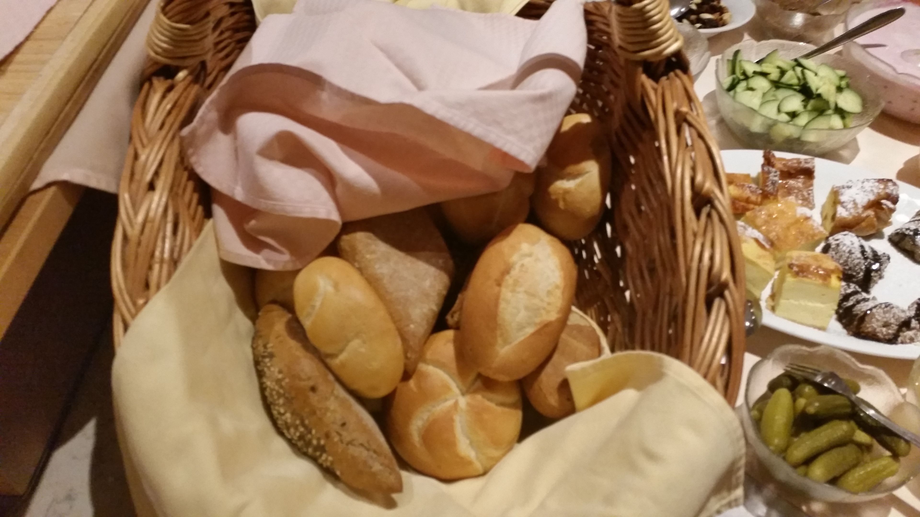 Een rieten mand gevuld met diverse broden en gebak, een schaal augurken, en een bord met kaas en noten.