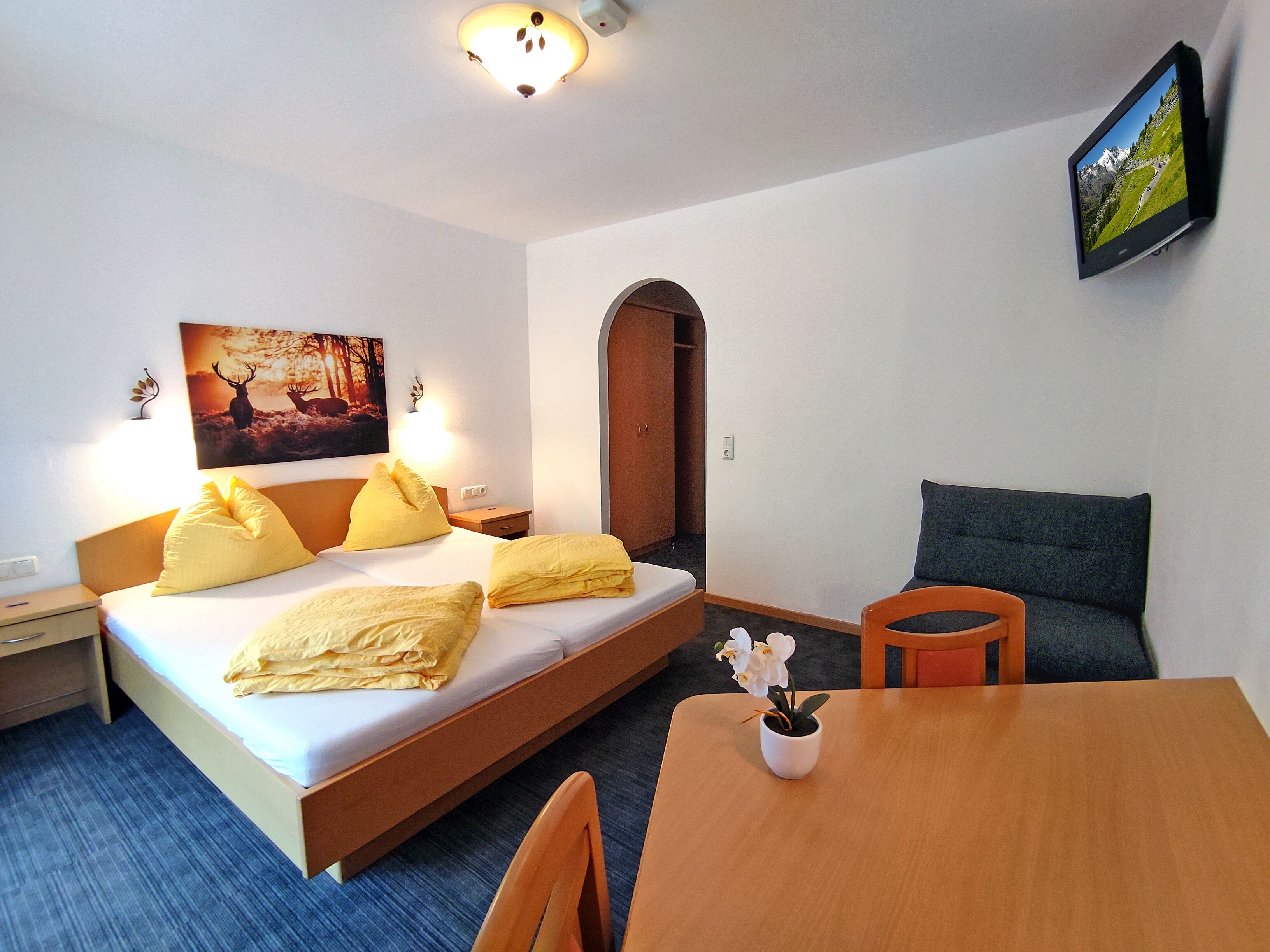 A hotel room with a bed, a desk, a chair, a TV, and a painting on the wall.