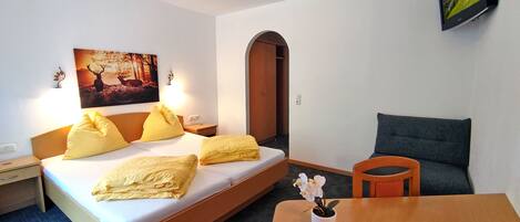 A hotel room with a bed, a desk, a chair, a TV, and a painting on the wall.