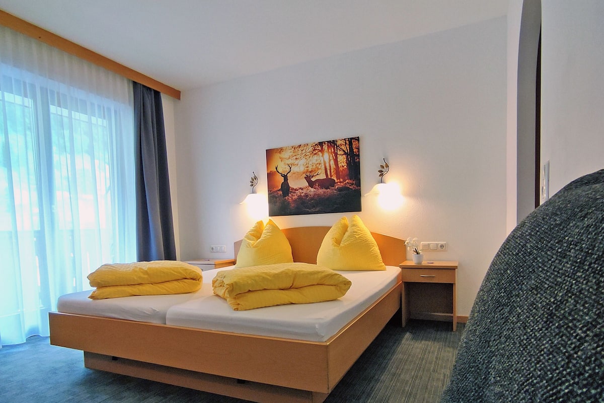 A modern hotel room with a large bed, a painting of deer, and a small desk with a lamp.