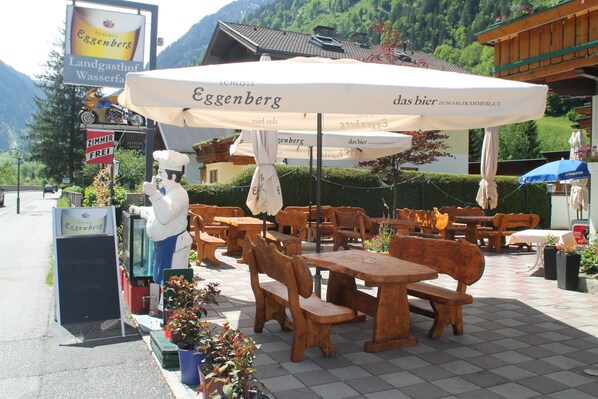 An outdoor seating area with wooden tables and benches, surrounded by potted plants and umbrellas. - Hotel Wasserfall (Fusch an der Grossglocknerstrasse)