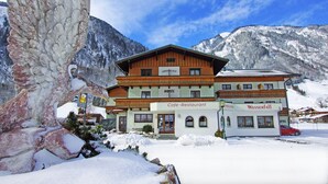 A hotel with a wooden facade, a sign indicating it's a cafe and restaurant, and a view of snow-covered mountains. - Hotel Wasserfall (Fusch an der Grossglocknerstrasse)
