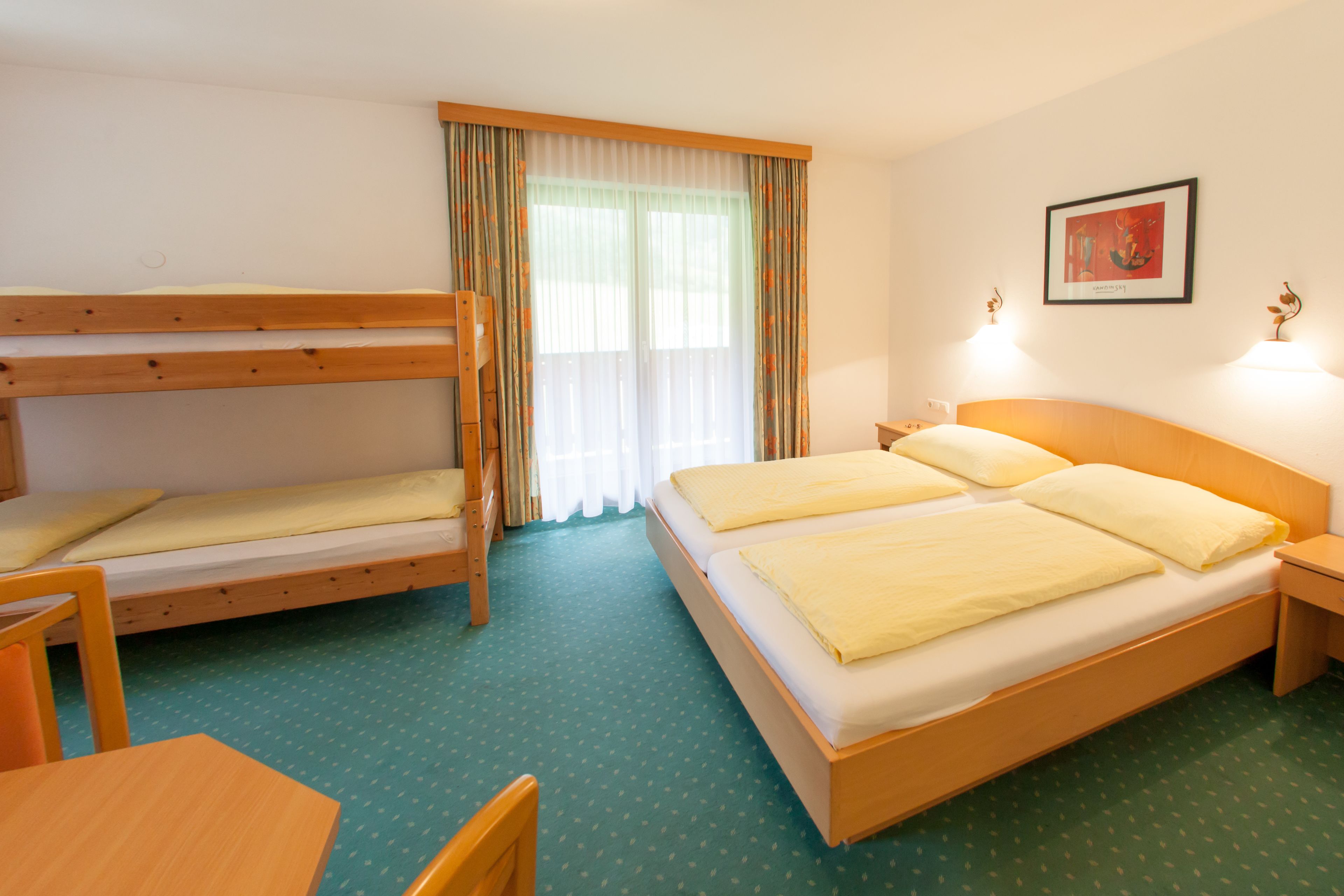A room with bunk beds, a single bed, a wooden table, and a framed picture on the wall.