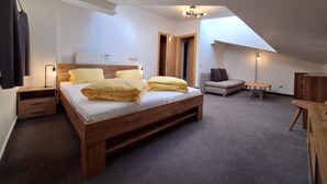 A bedroom with a wooden bed, a gray sofa, a small table, and a ceiling light fixture. - Hotel Wasserfall (Fusch an der Grossglocknerstrasse)