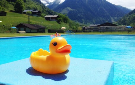 A swimming pool with a rubber duck in the foreground and a mountainous landscape in the background.
