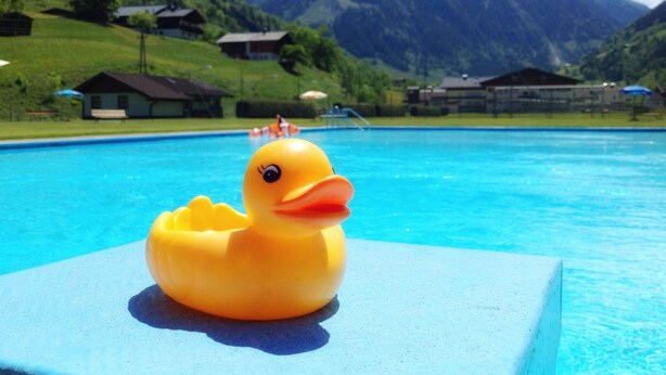 A swimming pool with a rubber duck in the foreground and a mountainous landscape in the background. - Hotel Wasserfall (Fusch an der Grossglocknerstrasse)