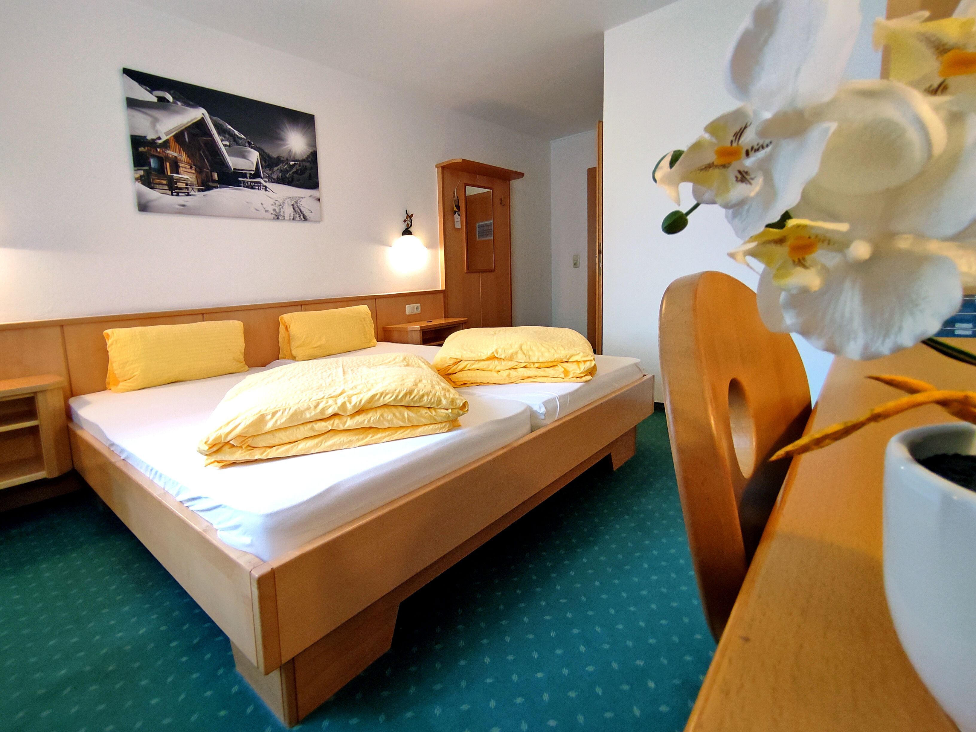 A hotel room with a wooden bed, a nightstand, a wooden wardrobe, and a wall-mounted picture.