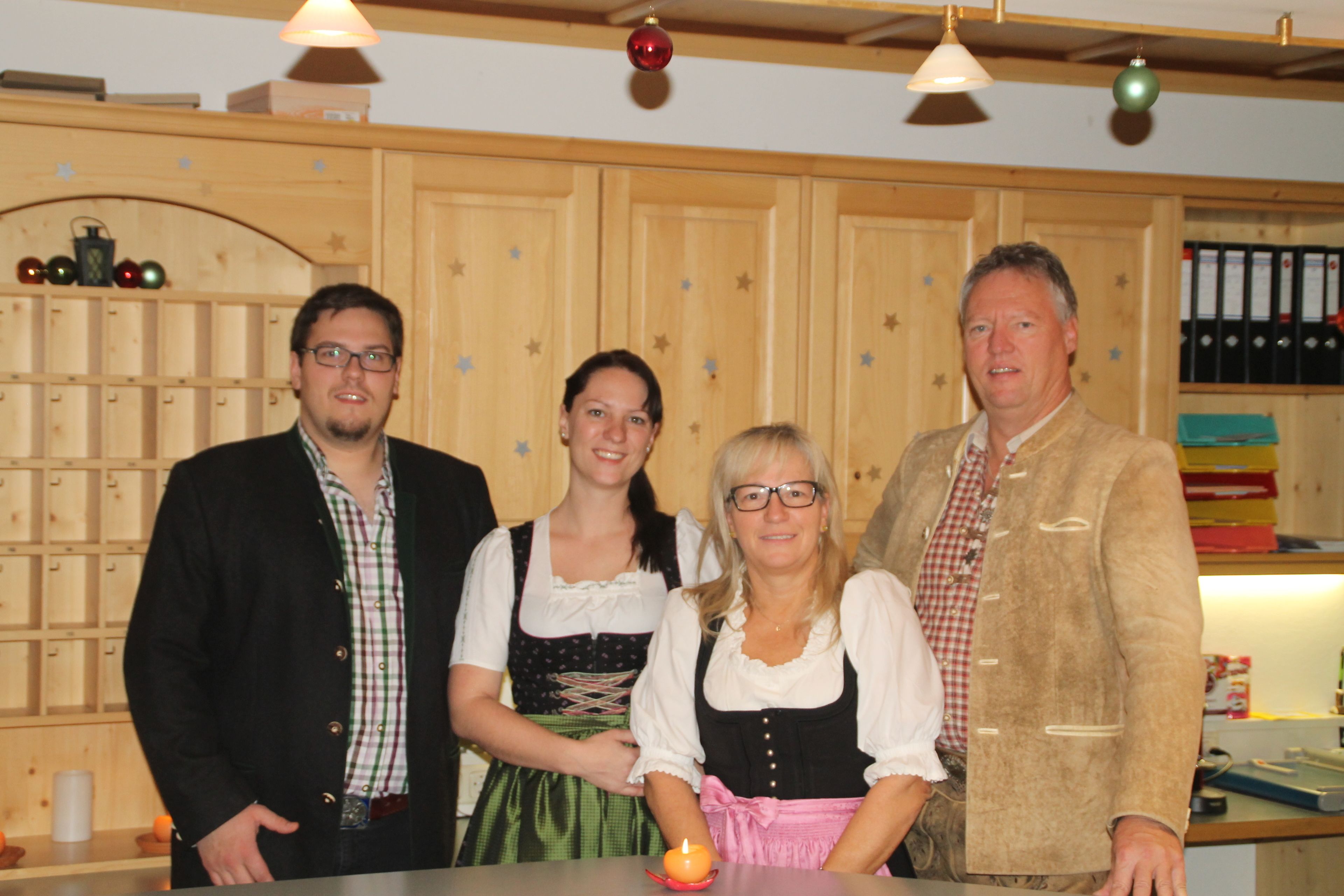 A group of people in traditional attire standing in a room with wooden paneling and a shelf with boxes.