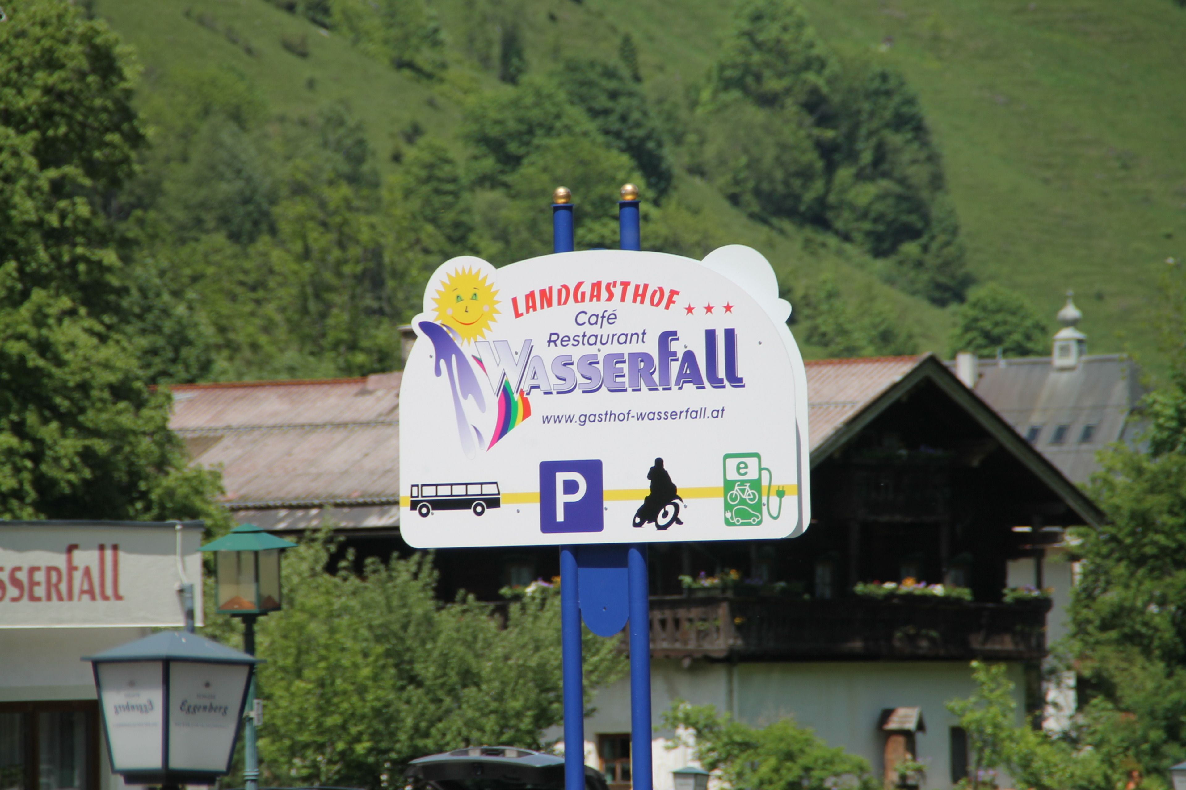 A sign for Landgasthof Café Restaurant Wasserfall with parking and electric vehicle charging symbols.